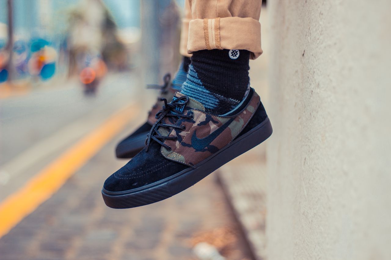 Home Crop anonymous child sitting on street with hanging feet in skate sneakers with camouflage details socks and trousers